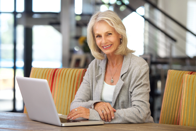 business starten mit 50: Selbstbewusste Frau über 50 sitzt lächelnd am Laptop und plant ihren beruflichen Neuanfang.